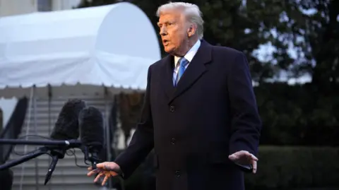 EPA Trump in blue overcoat and blue tie in front of microphones and near white canopy on White House driveway