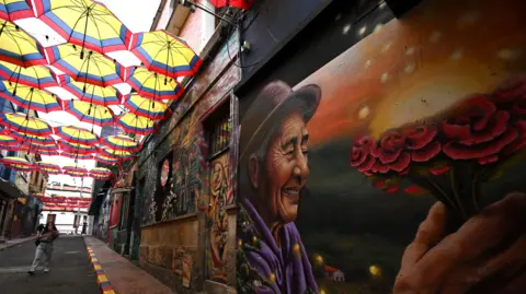 AFP via Getty Images A large mural of a man looking at a sunset on a street in Bogotá's historic Candelaria neighborhood.
