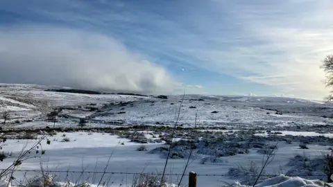 Snow covering the hills on Dartmoor, with blue and cloudy skies seen afar.