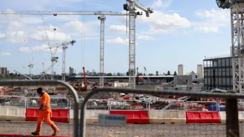 EPA A construction worker in fluorescent orange walks past cranes at HS2 Old Oak Common construction site in London