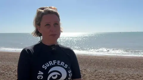 Clare Osborne stands on Brighton beach wearing a black Surfers Against Sewage t-shirt