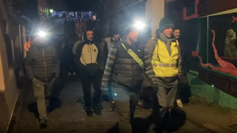 A group of men pictured walking in high vis jackets and head torches.