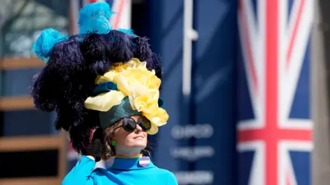PA Media/Andrew Matthews A woman wearing an elaborate fascinator, which is very tall and contains large feathers, which are light blue and dark blue.
