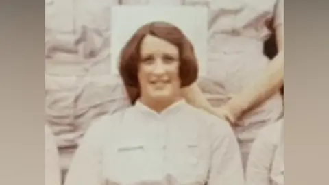 A historic sepia photograph of a female nurse in white uniform smiling at the camera.