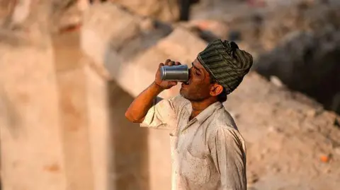 Getty Images A construction worker quenches his thirst as he takes a break, amid intense heat waves on a hot summer day on the banks of the Yamuna river, in New Delhi.