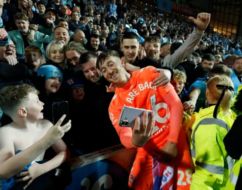 PA Media City's Josh Eccles in an orange away kit, takes a selfie with fans as they celebrate