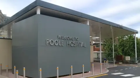 University Hospitals Dorset "Welcome to Poole Hospital" is spelled out on a large grey block in front of a canopied hospital entrance.
