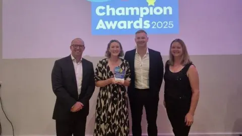 Cornwall Council Four people stand in a row as they accept the award. The group are standing in front of a screen which says living wage champions award 2025.