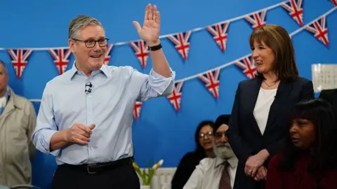 Getty Images Britain's Prime Minister Keir Starmer (L) speaks with guests as Chancellor of the Exchequer Rachel Reeves (R) looks on, during a visit to the Benn Partnership community centre in Rugby, in central England on 27 November 2025.