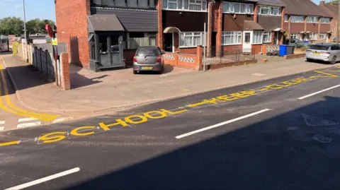 A street with a sign painted in yellow that reads School - Keep - Clear.