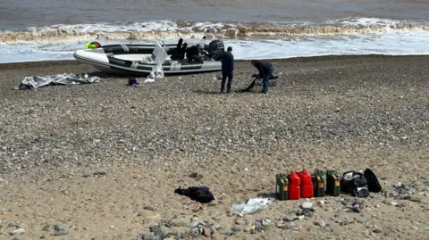 Small inflatable-type boat abandoned at Easington beach, close to the sea, with cannisters lined up in a row closer inshore