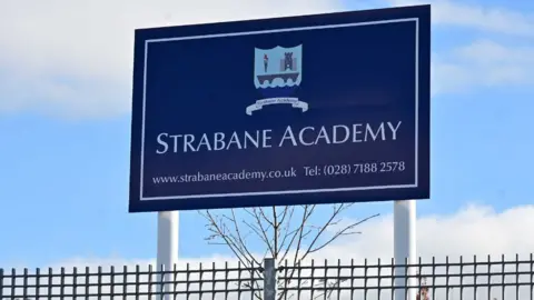 strabane academy blue signage with website details and photo number, pictured on poles above a fence with blue sky in background