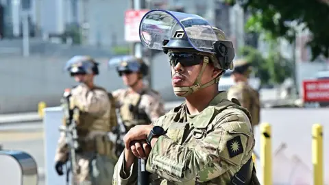 California National Guard troops standing in Los Angeles on 17 June, 2025. There is one in the foreground with his visor up and three in the background.