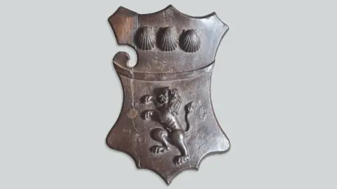 Hanson Ross A wooden coat of arms featuring a lion below three seashells.