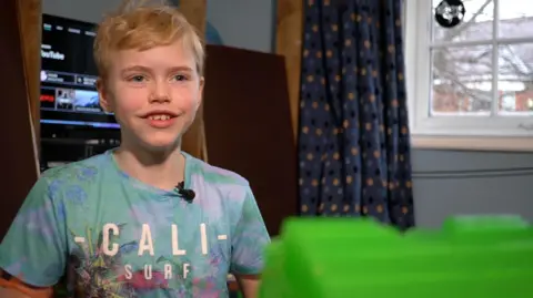 An 11-year-old Max Johnson, wearing a blue and green t-shirt with the logo Cali Surf, speaks to the camera