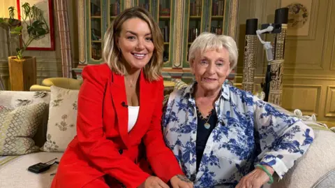 I Fought The Law recounts mum's double jeopardy murder law fight 1 BBC Sheridan Smith, left, wearing a red jacket and a white shirt sits on a beige sofa next to Ann Ming, right, who is wearing a black shirt underneath a white shirt which has blue coloured birds printed on it.