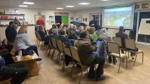 Sara Beecham A group of people sitting on chairs in a room, looking at a projector screen with a picture of the River Severn on it. A man standing by the projector appears to be running a presentation.