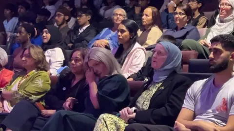Group of people in the theatre and Tatiana dabbing her eyes.