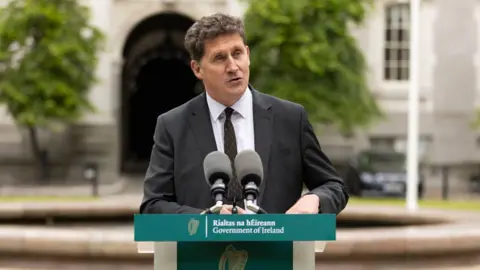 PA Media Eamon Ryan standing behind microphones with a blurred backdrop of Leinster House 