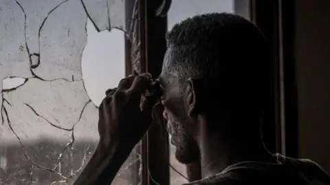 A Sudanese army soldier scans the frontline with binoculars in Khartoum North in December. He is looking out of broken window of a building.