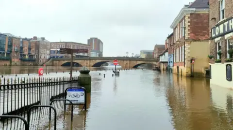 BBC Weather Watchers/Gary Gimmick A river spills out to the edge of buildings and is very high up to just below a bridge.