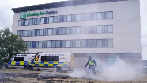 PA Media A police officer extinguishes a small fire during an anti-immigration demonstration outside the Holiday Inn Express in Rotherham, South Yorkshire.