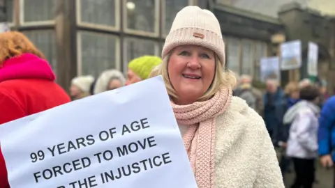 Justine Gibling, a campaigner at a rally in Belper, carrying a placard that reads: 99 years of age forced to move...the injustice'