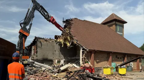 BBC a high-reach excavator tears down a building made of brick 