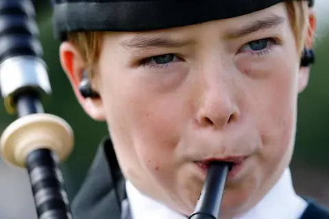 Getty Images A close-up of a young boy playing the bagpipes. His cheeks are puffed out as he blows into the mouthpiece