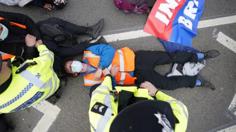 James Manning/PA Media An Insulate Britain protestor lying on the ground. He is being hand cuffed by police. 