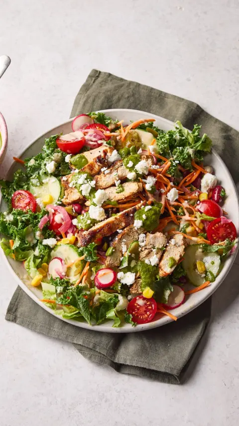 A white plate sits on a grey napkin. It contains a large salad with lots of different ingredients.