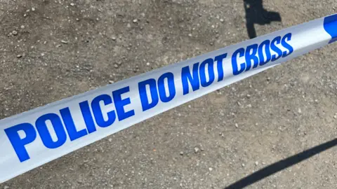 A strip of police tape. It reads, Police do not cross in blue writing on a white background 