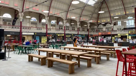 Inside the Market Hall where there are benches pictured and stalls visible in the background. 