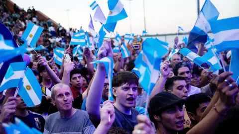 Getty Images Supporters of President of Argentina Javier Milei wave Argentine flags waiting for his arrival at a closing campaign rally ahead the mid-term election on October 23, 2025 in Rosario, Argentina