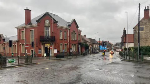 An image of a wet street with a red brick building on the corner of a junction.