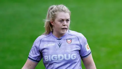 Sam Monaghan walking on the pitch wearing Gloucester-Hartpury kit