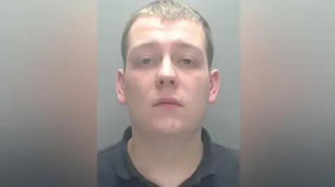 Mugshot of Thomas English. He is clean-shaven with short dark hair and is wearing a black polo shirt