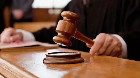 A hand is holding a gavel over a sound block in a court room