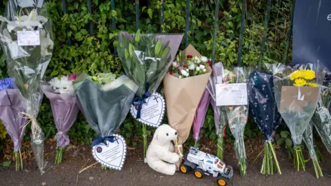 Getty Images Several bouquets of flowers laid in tribute to a boy who died. Many of them include notes and cards. There is also a teddy and a toy car on the ground.