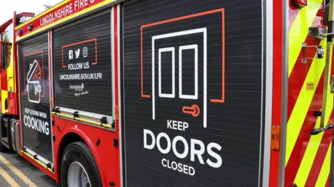 Side view of a Lincolnshire Fire and Rescue engine with the sign 'keep doors closed' on the side