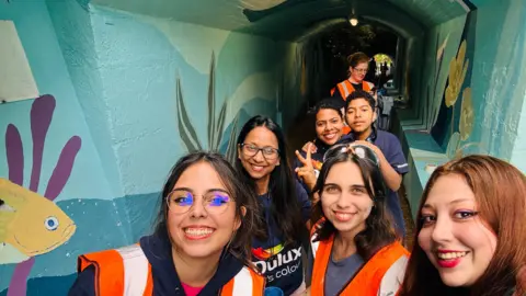 Viva Slough Volunteers smiling in a tunnel painted with an under-the-sea theme.