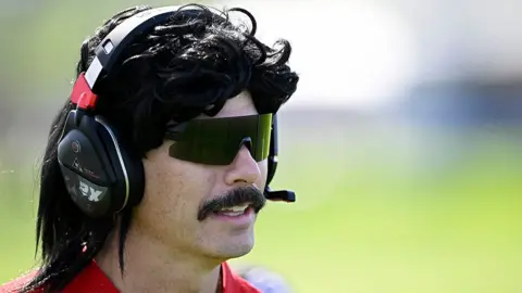 Getty Images Content creator Dr Disrespect at a golf tournament, wearing a red tshirt and a black and red headset.