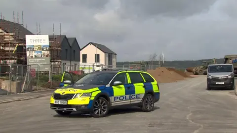 Police car in the Rivenwood housing estate, where army personnel use excavators to pile sand on the explosive device before planning a controlled explosion.