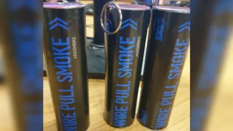 Gloucestershire Police Three black cylindrical flare cannisters with blue writing that says 'wire pull smoke'