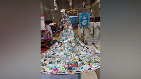 Coat of Hopes A person is wearing a long patchwork coat which is draped across the floor of a church. 