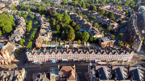 An aerial view of about 100 terraced houses on three different streets with some trees dotted about