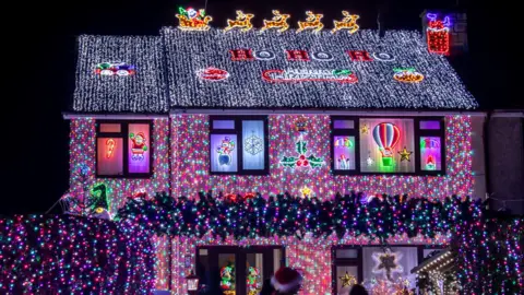 Simon Boddy/Ambitious PR A house is covered in illuminated Christmas lights at Winterbourne near Bristol, many of them blue and purple. There are lit-up letters on the roof that spell out Ho Ho Ho.