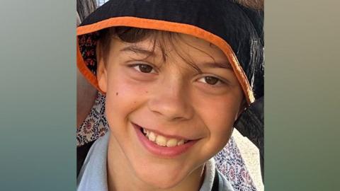 A smiling 11-year-old boy wearing a rain hat 