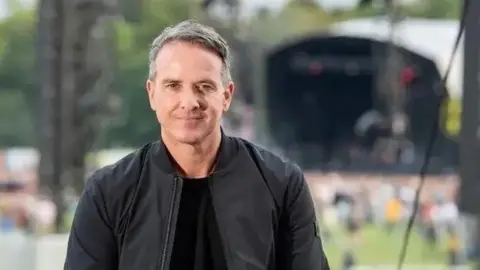 Darren Robinson Sacha Lord wears a black bomber jacket and t-shirt while stood in front of a crowd of people at Parklife festival 