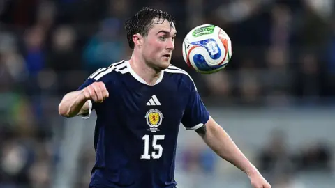 Getty Images John Souttar is an adult in a Scotland strip. The number 15 is on the front. He is about to head a ball.